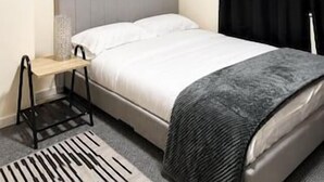 A bedroom with a bed, a bedside table, a black curtain, and wall art.