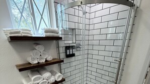 Une douche d’angle avec des carreaux de céramique blancs rectangulaires, une porte en verre et un tapis de bain bleu.