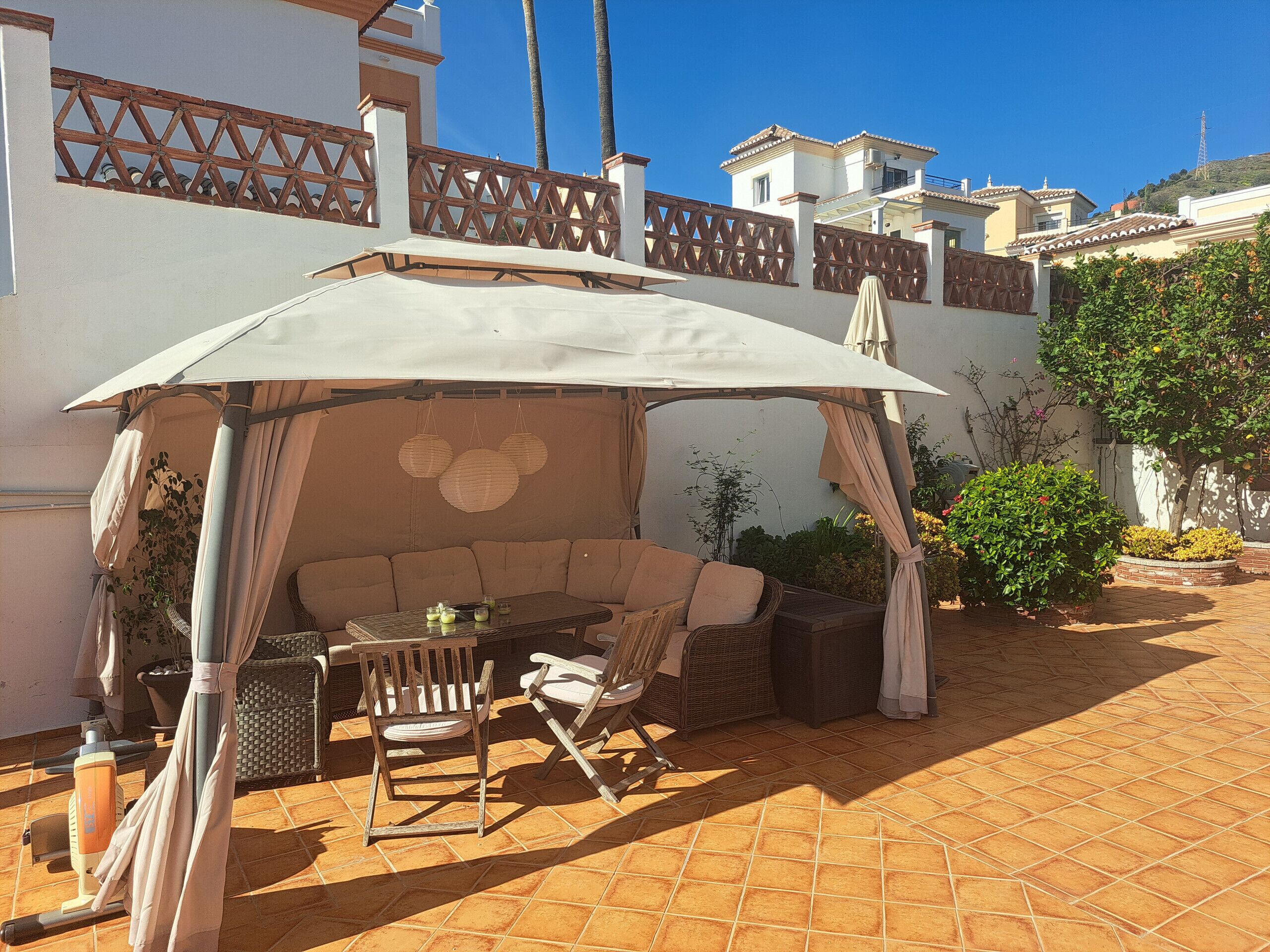 Une terrasse extérieure dotée d’un espace salon couvert, comprenant un canapé et des fauteuils, ainsi qu’une table avec des boissons.