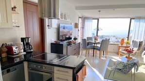 A modern kitchen with a central island, a dining area with a view, and a living space with a sofa and table. - Las Mimosas 7B Capistrano Village in Nerja (Nerja)