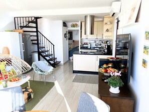 Eine moderne Küche mit Einbauofen, Mikrowelle und Kaffeemaschine. Ein Essbereich mit Tisch und Stühlen sowie eine Treppe, die zu einer oberen Ebene führt.
