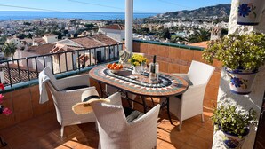 A terrace with a tiled floor, wicker furniture, a table with a decorative centerpiece, and potted plants. - Las Mimosas 7B Capistrano Village in Nerja (Nerja)