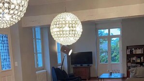 A dining area with a long table, chairs, a chandelier, a TV, and a bookshelf.