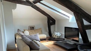 A loft-style room with exposed wooden beams, a sofa, a TV, and a dining table.