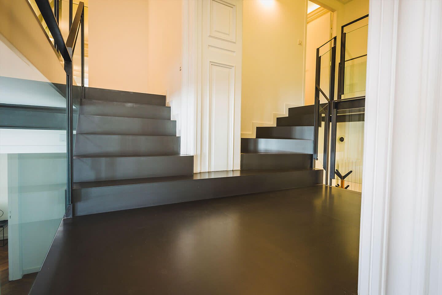 En moderne trappe med glasgelændere og mørkt gulv.