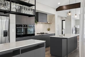 A modern kitchen with a central island, built-in oven, and stainless steel appliances. - Coastal Luxe in Seaside Estate | 4 Bedrooms | Walk to Beach (Mandurah)