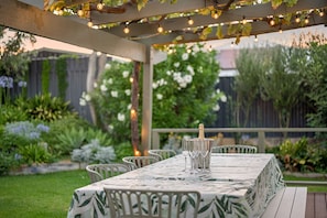 Eine Terrassengruppe im Freien mit Esstisch, umgeben von viel Grün und Lichterketten.