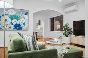 Ein modernes Wohnzimmer mit einem grünen Sofa, einem großen Blumenbild, einem Topfpflanzen und einem Fernseher.