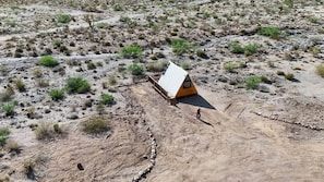 Un piccolo edificio a un piano con tetto spiovente, immerso in una vegetazione rada in un ambiente desertico.