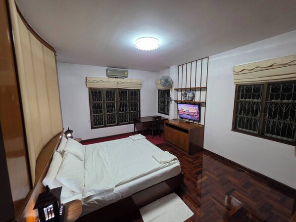 A bedroom with a bed, a desk with a TV, a fan, and a window with decorative grills. - Entire Home at Racha Herb Gardens 5br, Sleeps 11 (Saraphi)