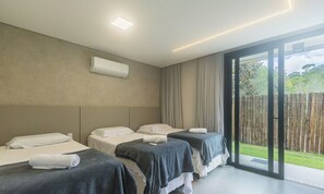 A hotel room with three beds, a sliding glass door to the outside, and an air conditioning unit on the wall. - Condo w/ Pool 600m From the Beach in Arraial D'ajuda - CRP (Porto Seguro)