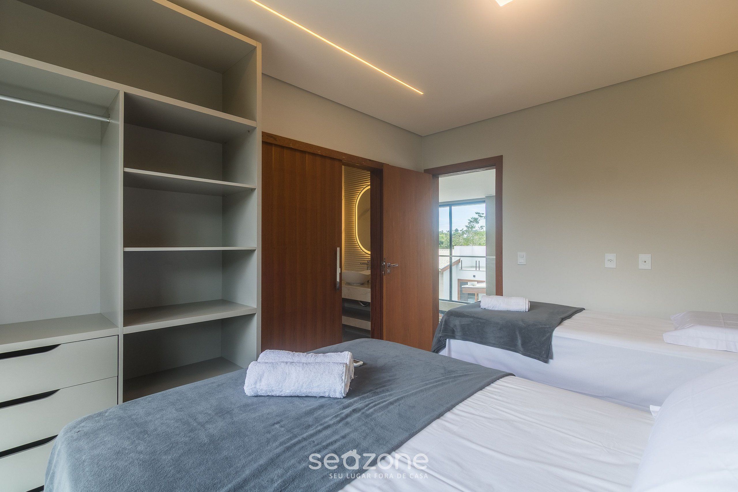A modern hotel room with a large wardrobe, two beds, and a view through an open door.