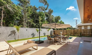 Un patio al aire libre con piscina, sillones de descanso y una mesa de comedor con sillas.