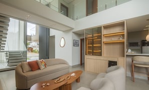 A modern living room with a sofa, a wooden coffee table, and a kitchen area with a microwave and refrigerator.