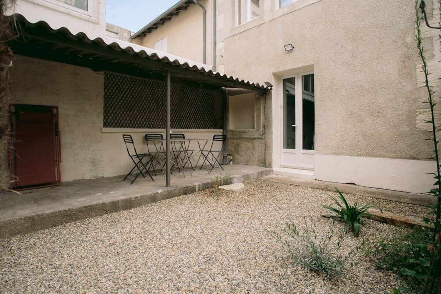 A covered patio with a table and chairs, a door, and a small garden area.