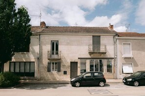 A two-story building with a tiled roof, a balcony on the second floor, and a car parked in front. - Georges' Journey - 154 (Périgueux)