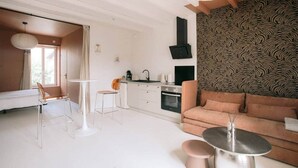 Ein modernes Wohnzimmer mit einer Couch, einem Esstisch und Stühlen. Es gibt eine Küchenzeile mit einem Herd und einem Spülbecken.