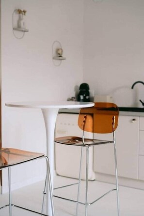 A modern kitchen with white cabinets, a white countertop, a white table, and a glass chair. - Georges' Journey - 154 (Périgueux)
