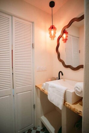 A bathroom with a white sink, a mirror with a wavy frame, and a hanging light fixture. - Georges’ Garden – 151 (Périgueux)