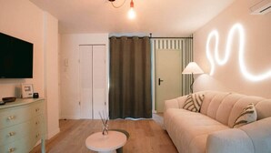 Un salon comprenant un canapé, un téléviseur, une lampe, une petite table et une porte donnant sur une autre pièce.