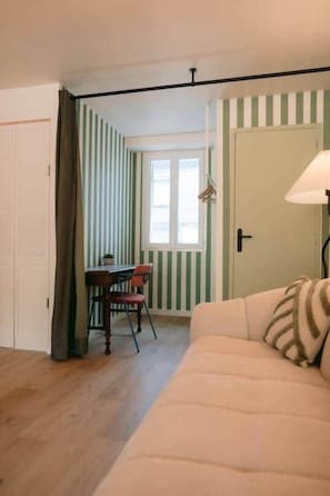 A room with a striped wall, a wooden floor, a sofa, a table with chairs, and a door. - Georges’ Garden – 151 (Périgueux)