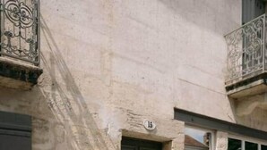 Un bâtiment en pierre avec une porte sombre, une fenêtre et un balcon doté de rampes en métal.