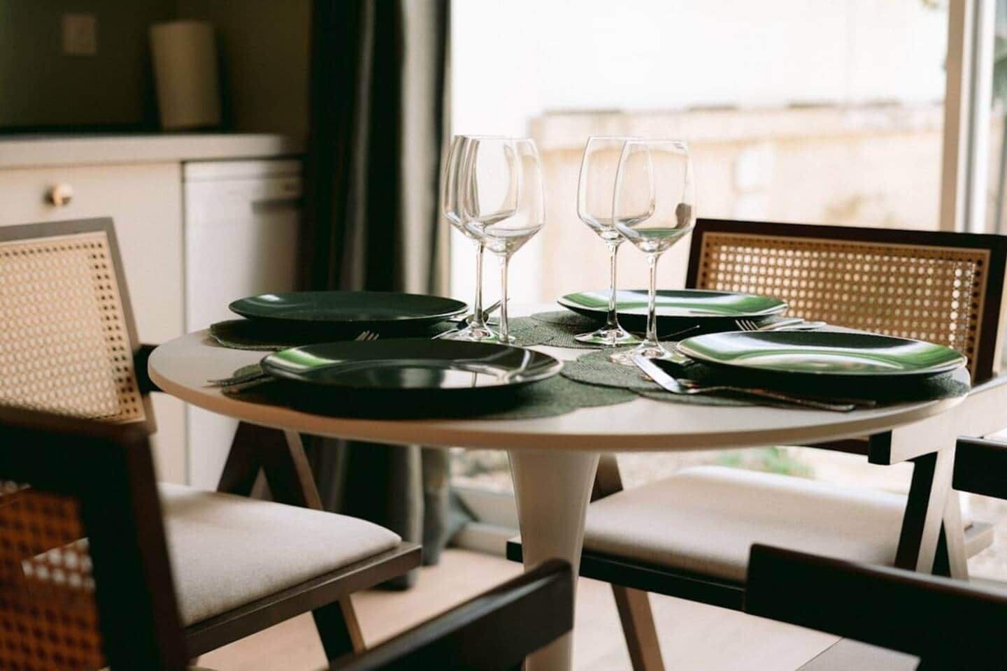 A dining table set with plates, cutlery, and glasses, surrounded by chairs.