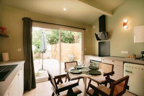A compact kitchen with a dining area, a sliding glass door to the outside, and a small refrigerator. - Georges’ Garden – 151 (Périgueux)