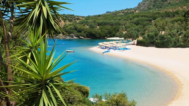 Ein Strand mit klarem türkisblauem Wasser, einem Sandstrand und einer Reihe von Sonnenschirmen.