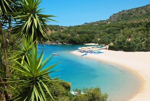 Ein Strand mit klarem türkisblauem Wasser, einem Sandstrand und einer Reihe von Sonnenschirmen.