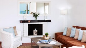 Ein Wohnzimmer mit Kamin, einem weißen Sessel, einem braunen Sofa und einem Couchtisch mit einem Buch.