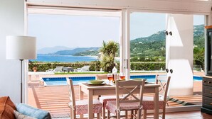Ein Zimmer mit Blick auf Pool und Berge, ein Esstisch mit Stühlen und eine Couch.