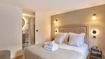 Quarto moderno com uma cama grande, duas luminárias de cabeceira, uma mesinha de cabeceira pequena e um painel de parede de mármore.