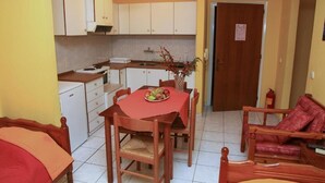 A compact kitchen with white cabinets, a dining table with chairs, and a red tablecloth. - Argo apartments near Nafplio (Nea Kios)