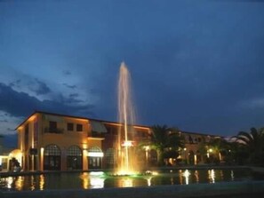 A building with a fountain in front, a pool, and palm trees. - Argo apartments near Nafplio (Nea Kios)