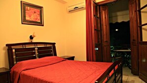A bedroom with a wooden bed, a nightstand, a framed picture on the wall, and an open door leading to a balcony. - Argo apartments near Nafplio (Nea Kios)