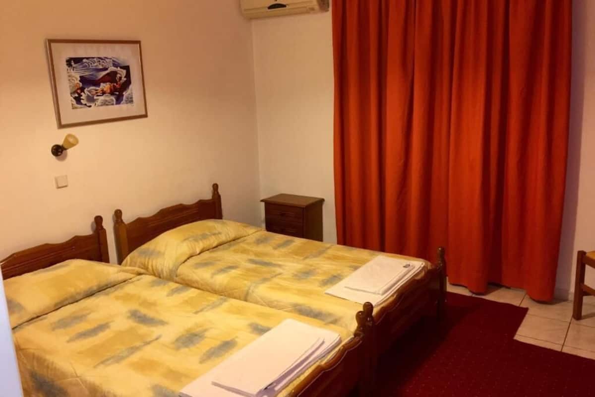 Een slaapkamer met twee bedden, een rood gordijn, een klein nachtkastje en een lijst met een afbeelding aan de muur.