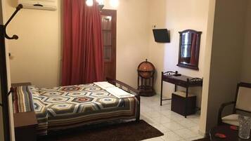 A bedroom with a bed, a desk, a chair, a lamp, a TV, and a window.