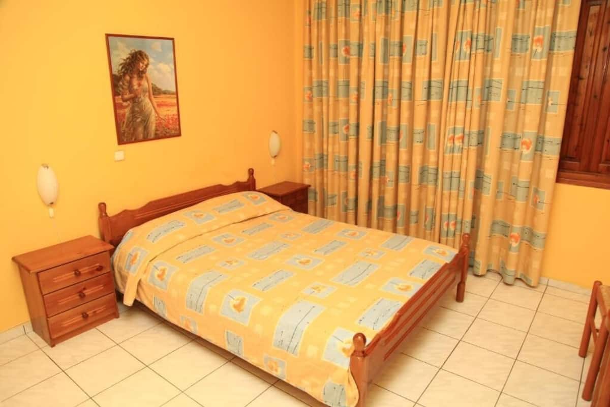 Een slaapkamer met een houten bed, nachtkastje, dressoir en een schilderij aan de muur.