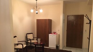 A small, cozy room with a dark brown rug, a wooden wardrobe, a white refrigerator, and a door with a coat rack. - Argo apartments near Nafplio (Nea Kios)