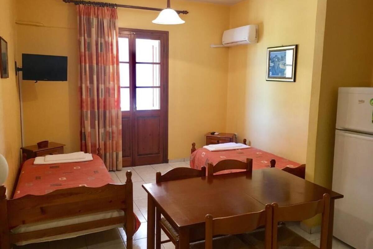 Een kamer met twee bedden, een eettafel, een televisie, airconditioning en een koelkast.