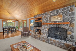 Un salon chaleureux avec une cheminée en pierre, un plafond en bois et de grandes fenêtres.