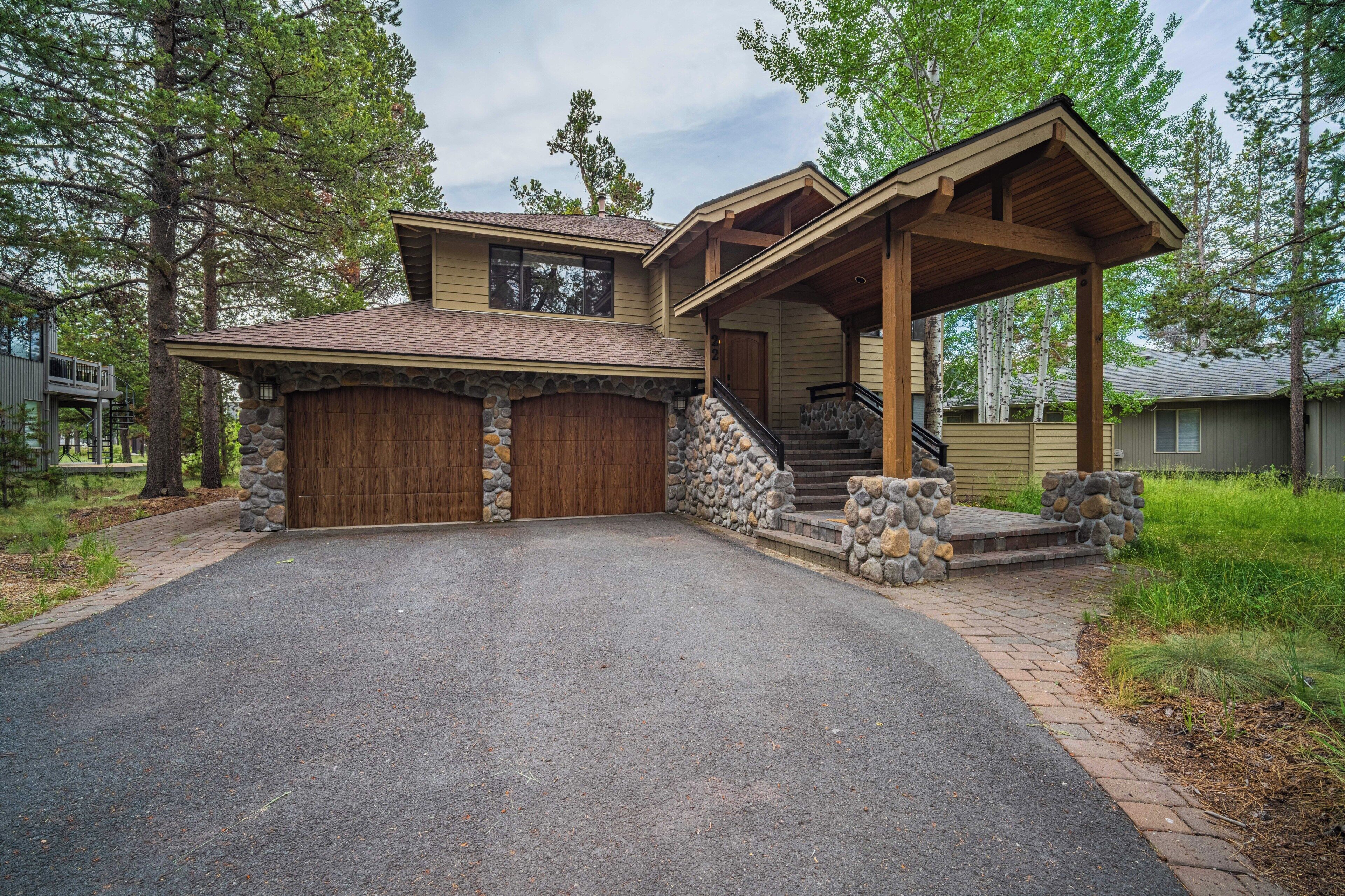 A charming mountain-style home with stone accents, warm wood details, and a covered entrance sits nestled among tall pines, offering a peaceful retreat in a tranquil wooded neighborhood.