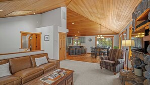 A spacious living room with a wooden ceiling, a brown leather sofa, a coffee table with magazines, a stone accent wall, and a dining area with a bar. - Quiet Sunriver Retreat with Access to Exclusive Golf (Sunriver)