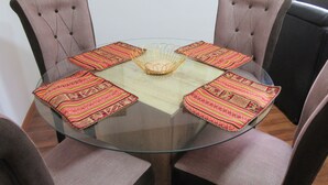 A round glass table with a woven centerpiece, surrounded by four upholstered chairs with patterned cushions.