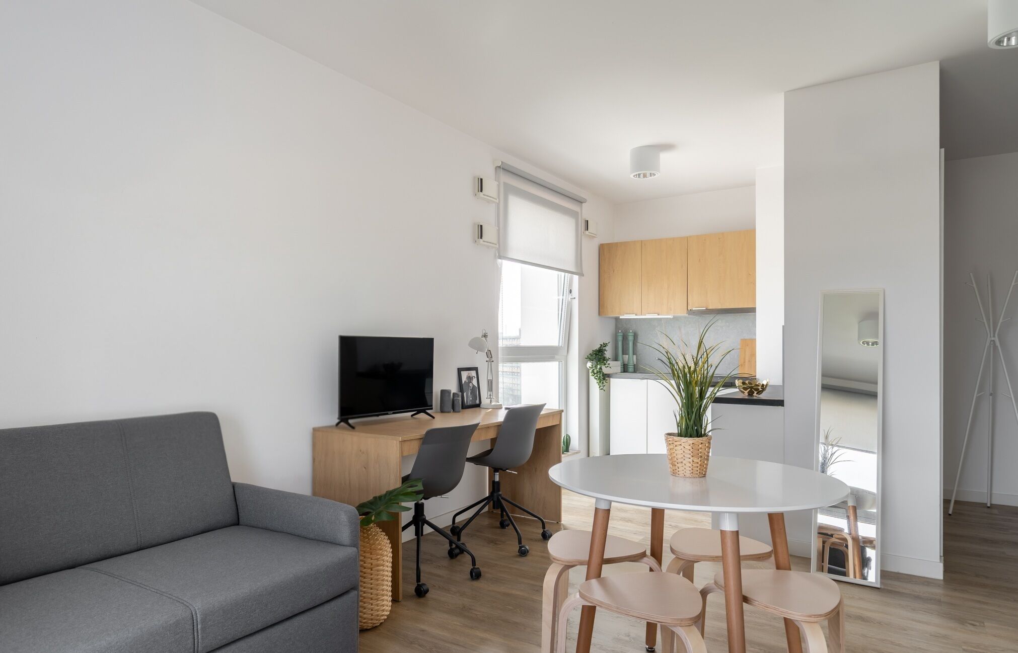 Una sala de estar moderna con un sofá gris, un televisor, una mesa de comedor con sillas y una cocina al fondo.