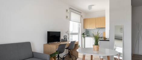 Una sala de estar moderna con un sofá gris, un televisor, una mesa de comedor con sillas y una cocina al fondo.