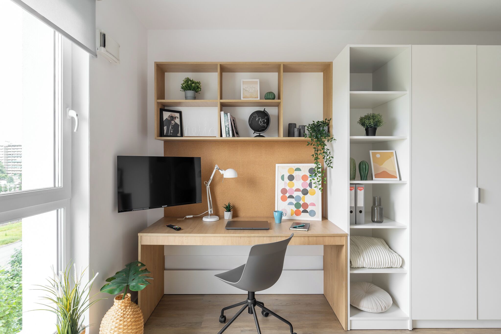 Un espace de bureau moderne comprenant un bureau, une chaise, un téléviseur et des étagères ornées de plantes et de livres.