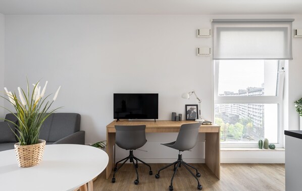Un espacio de oficina moderno con un escritorio, dos sillas, un televisor, una lámpara y una ventana con vistas a la ciudad.
