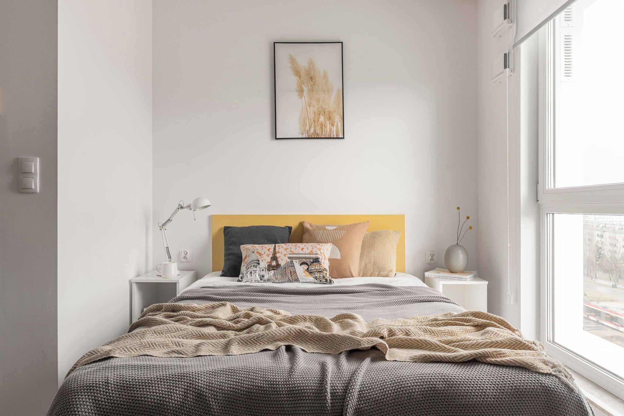 Een slaapkamer met een bed, nachtkastjes, een lamp, een ingelijst beeld en een raam.